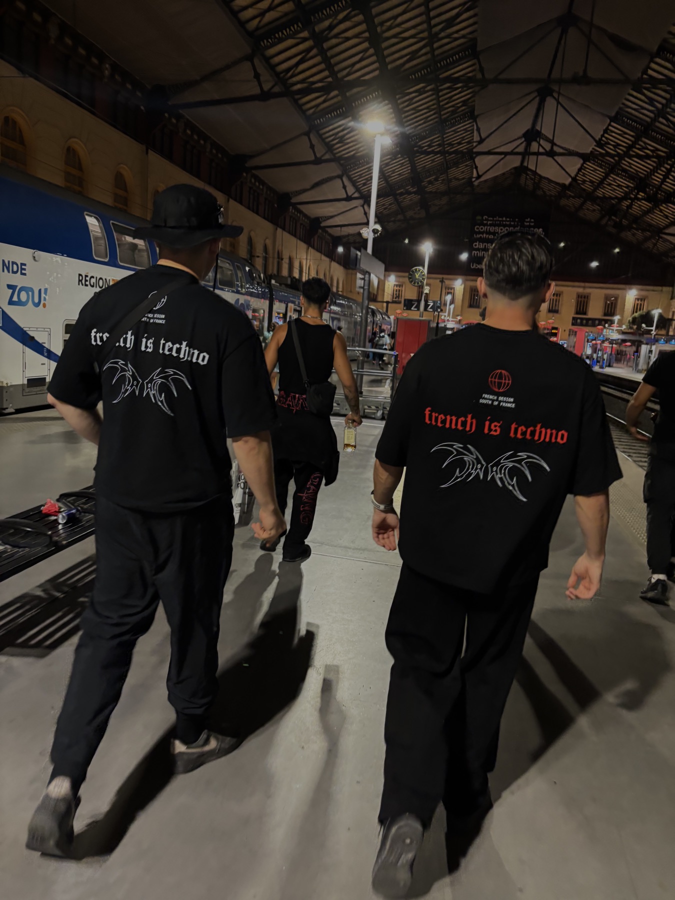 Une bande en t-shirts French is Techno marche sur un quai de gare la nuit